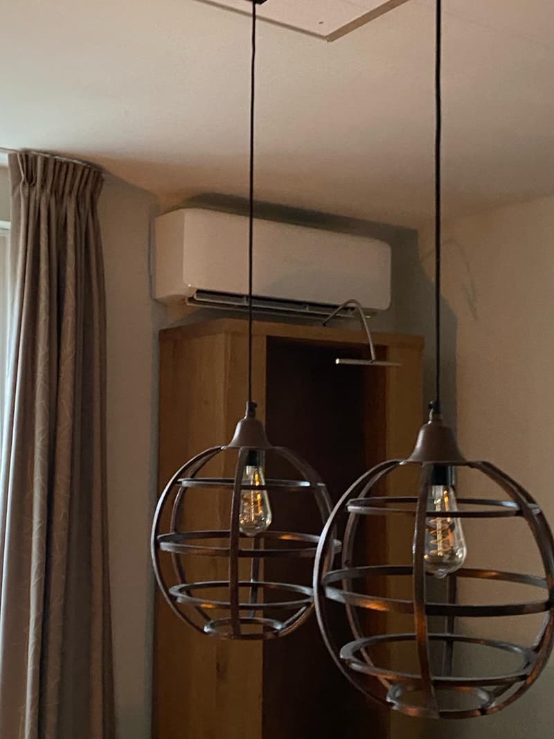 Wit wandmodel airco boven een kast in een eetkamer met hanglampen