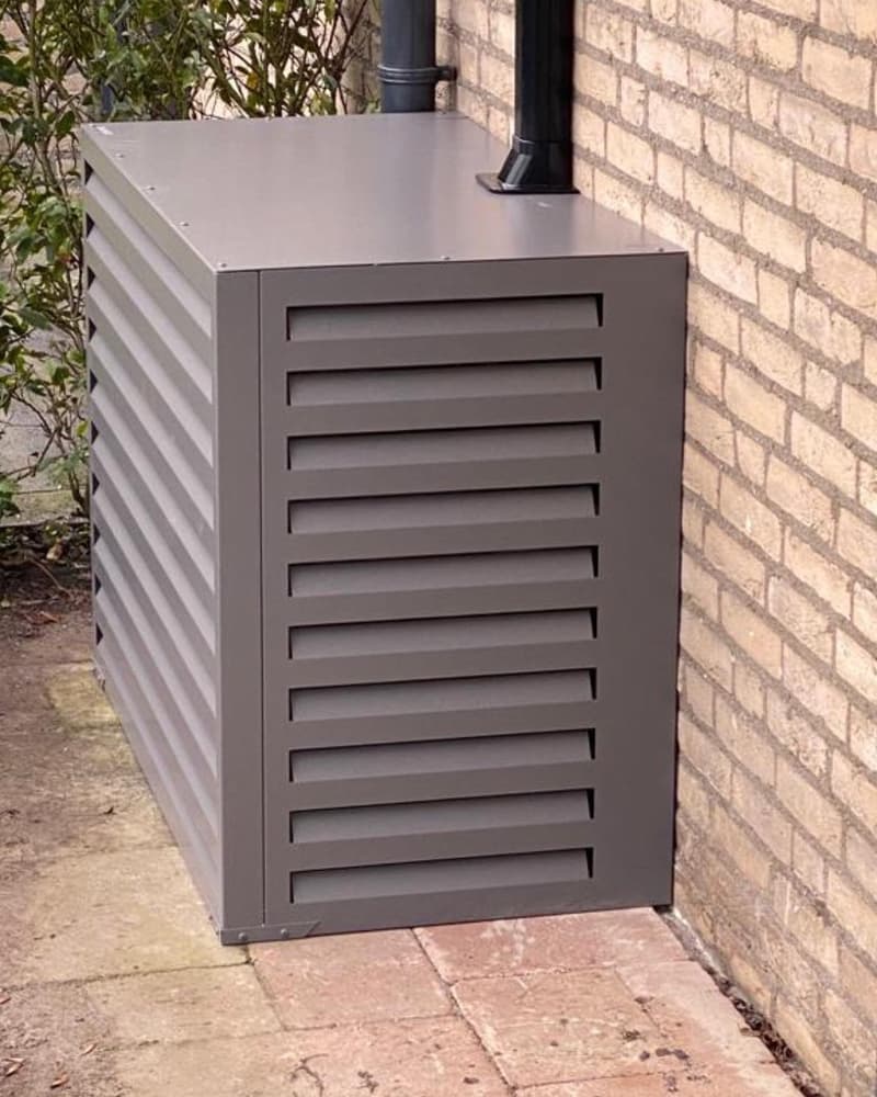 Buitenunit met grijze omkasting tegen een bakstenen gevel