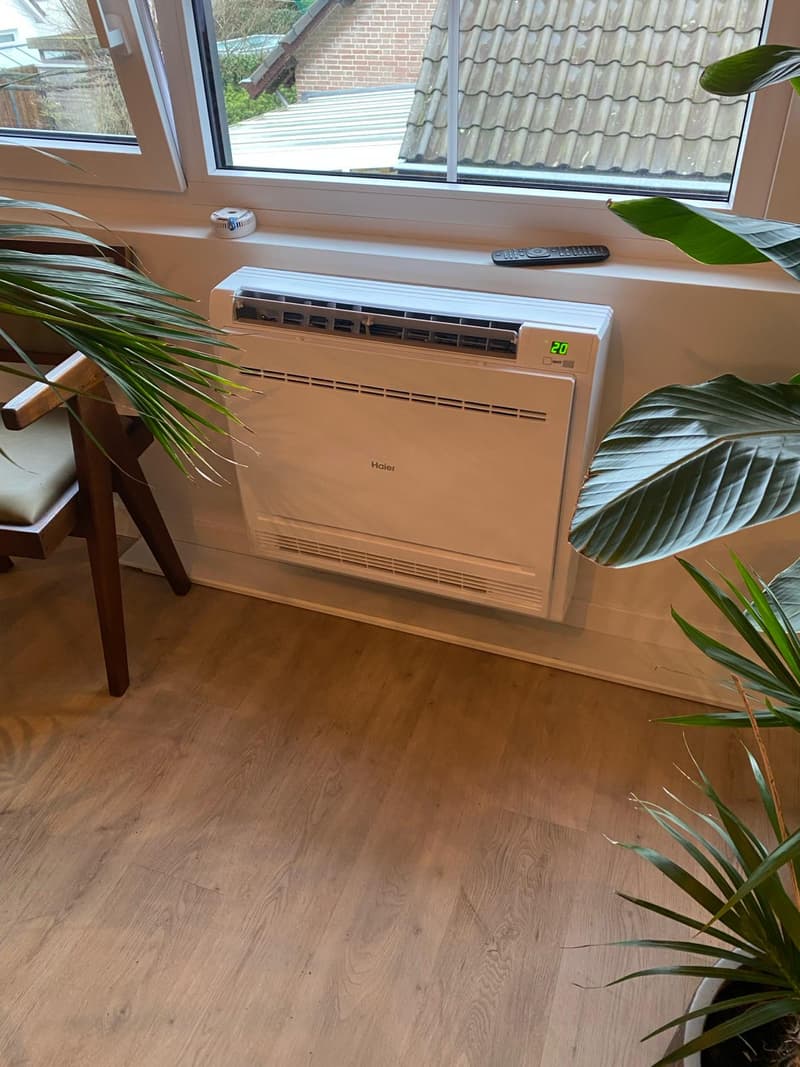 Console airco vloermodel onder een raam met planten